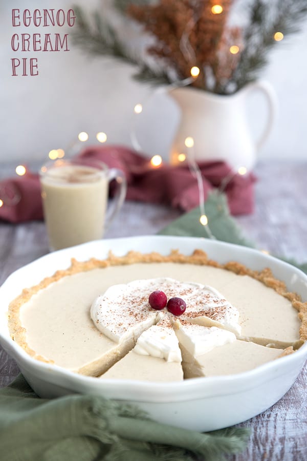 Keto Eggnog Pie in a white pie plate with holiday lights in the background.
