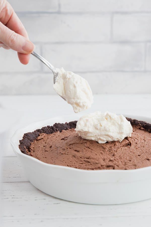 A spoonful of whipped cream being dolloped onto a keto chocolate mousse pie. 