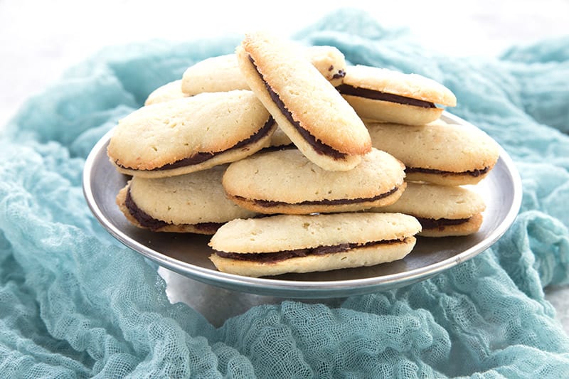 A silver plate of homemade milano cookies on a gauzy teal napkin. 