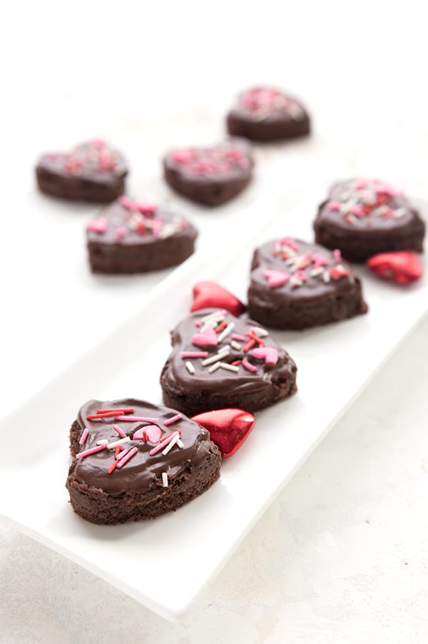 Coconut flour brownies cut into heart shapes on a white platter with Valentine's sprinkles. 