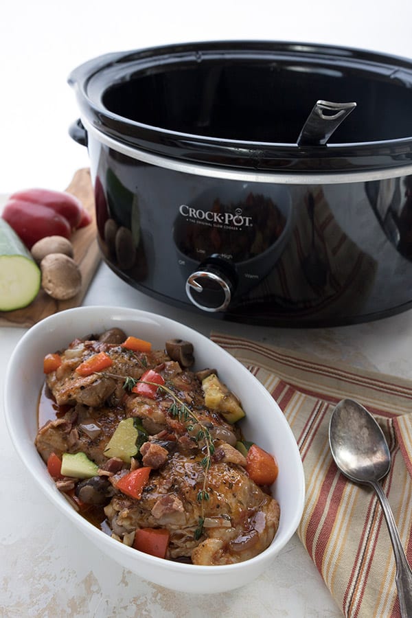 A white serving dish filled with chicken stew in front of a crockpot 
