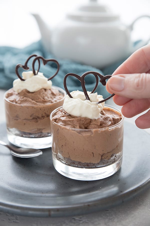 A hand reaching in to place little decorative chocolate hearts on a mini keto French silk pie. 