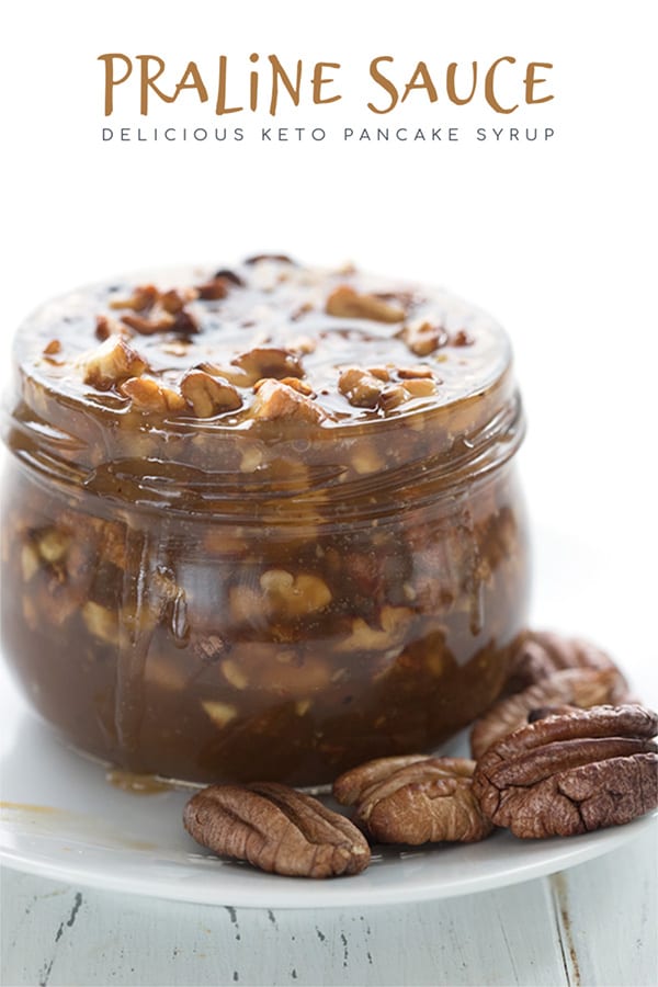 Keto praline pecan sauce in a jar on a white plate, with pecans around it. 