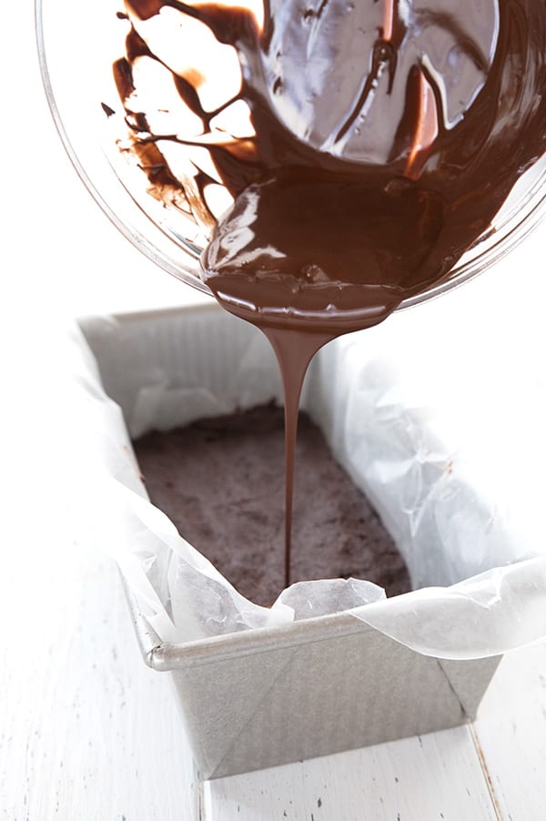 Pouring sugar-free chocolate over no bake brownies in a pan. 