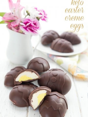 Keto easter creme eggs in a pile on a white table. A vase of flowers and a plate of chocolate eggs in the background.