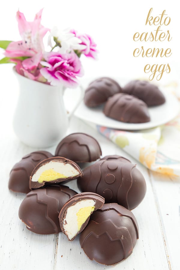 Keto easter creme eggs in a pile on a white table. A vase of flowers and a plate of chocolate eggs in the background. 