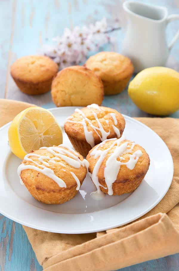 Keto lemon muffins on a white plate with lemons in the background. 