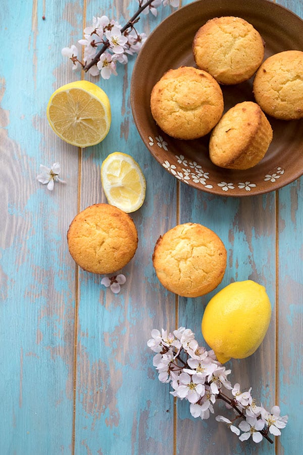 Top down photo of keto lemon cream cheese muffins on a brown plate on a blue table. Lemons and cherry blossoms around. 