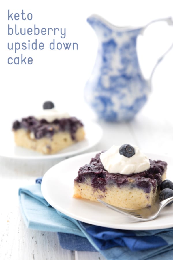 Two slices of blueberry upside down cake on white plates on a white table. A blue patterned jug sits in the background.