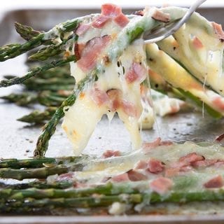 A fork pulling cheesy asparagus up from a baking sheet