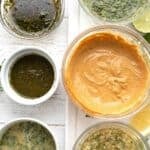 Titled image top down of 6 keto chicken marinades in small bowls on a white wooden table.