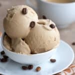 Two scoops of Keto Coffee Ice Cream in a white bowl with coffee beans sprinkled on top.