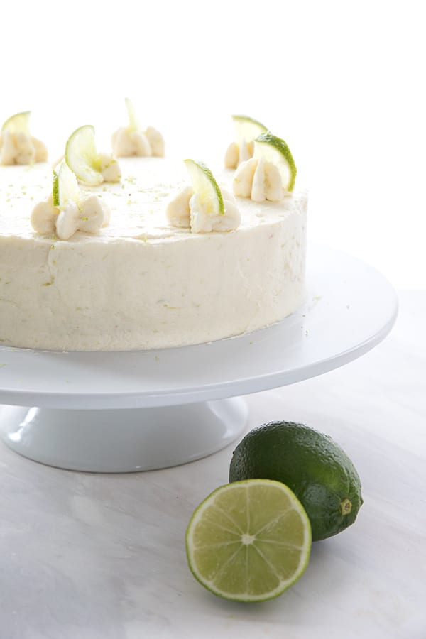 The whole keto margarita cake on a cake platter with two limes in front.