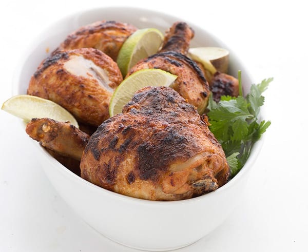 Tandoori chicken in a white oval dish with cilantro and slices of lime