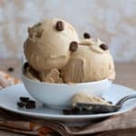 Two scoops of keto coffee ice cream in a white bowl, with a spoonful in front on the plate.
