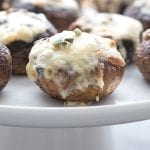 A cake plate with keto stuffed mushrooms filled with cheddar, garlic, and sage.