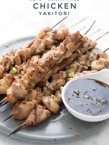Titled image of keto chicken yakitori skewers on a grey plate with a white dish of yakitori sauce