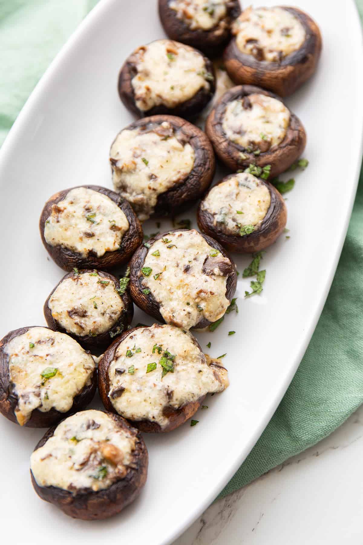 Cheesy Stuffed Mushrooms on a white oval platter over a pale green napkin. 