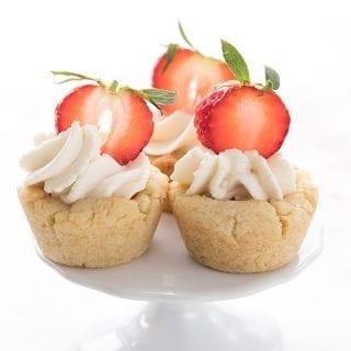 Three keto cookie cups filled with whipped cream and strawberries on a small cake stand.