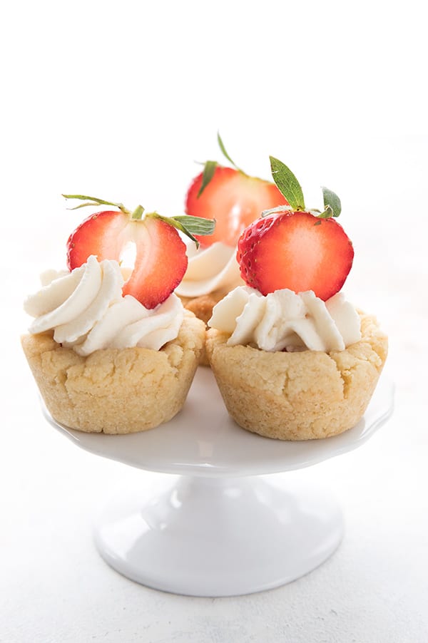 Three keto cookie cups filled with whipped cream and strawberries on a small cake stand.