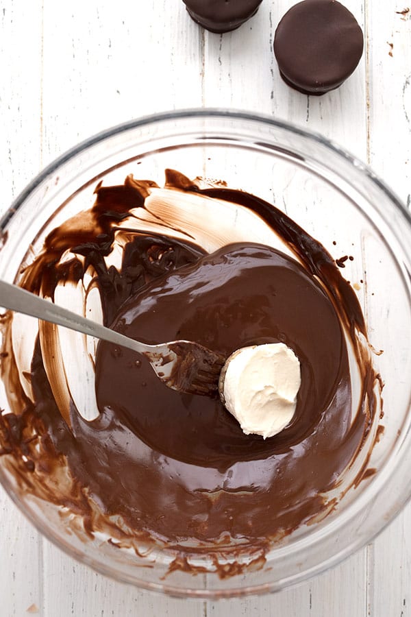 Top down photo of a keto cheesecake bite being dipped into melted chocolate