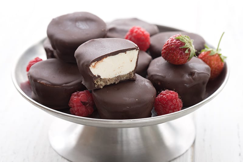 A metal cake tray filled with chocolate covered keto cheesecake bites and fresh strawberries and raspberries