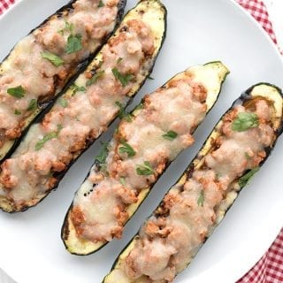 Top down photo of stuffed zucchini boats on a white plate over a red checked napkin