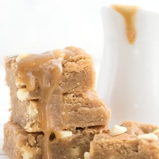 Keto white chocolate blondies in a stack with caramel sauce dripping down, with the pitcher of caramel sauce in behind.