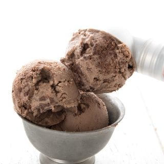 A scoop of keto Nutella ice cream being placed into a pewter bowl on a white wooden table