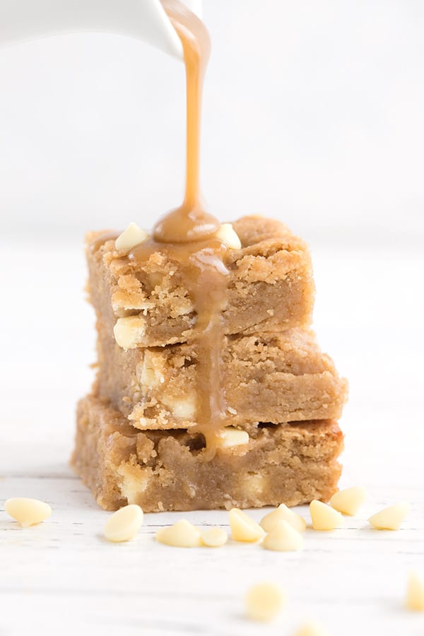 Keto caramel sauce pouring over low carb white chocolate blondies on a white background.