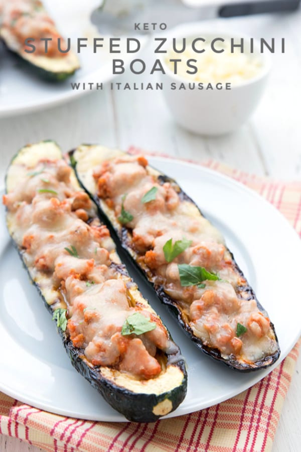 Titled image of keto grilled zucchini boats on a white plate, stuffed with Italian sausage, tomato sauce, and cheese.