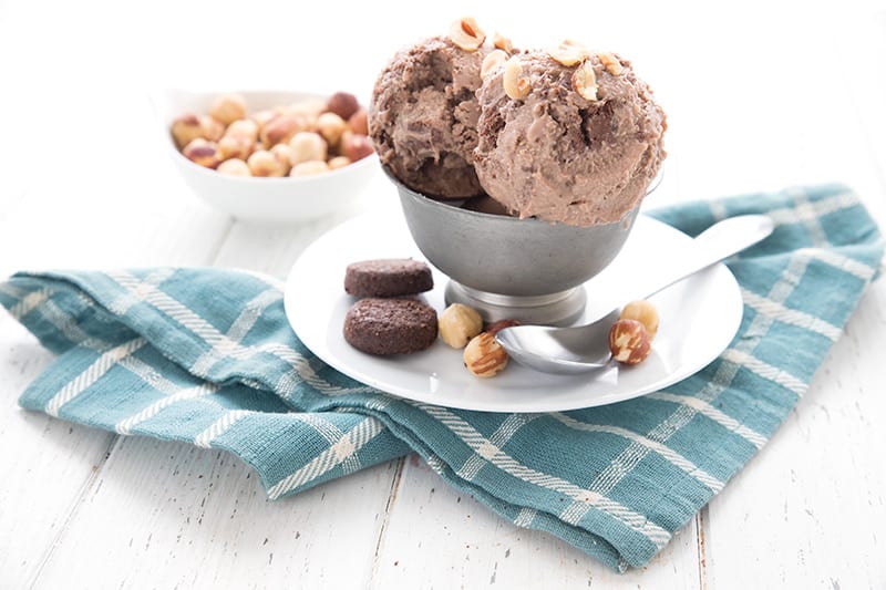 Chocolate hazelnut ice cream in a pewter bowl over a white plate, over a blue plaid napkin.