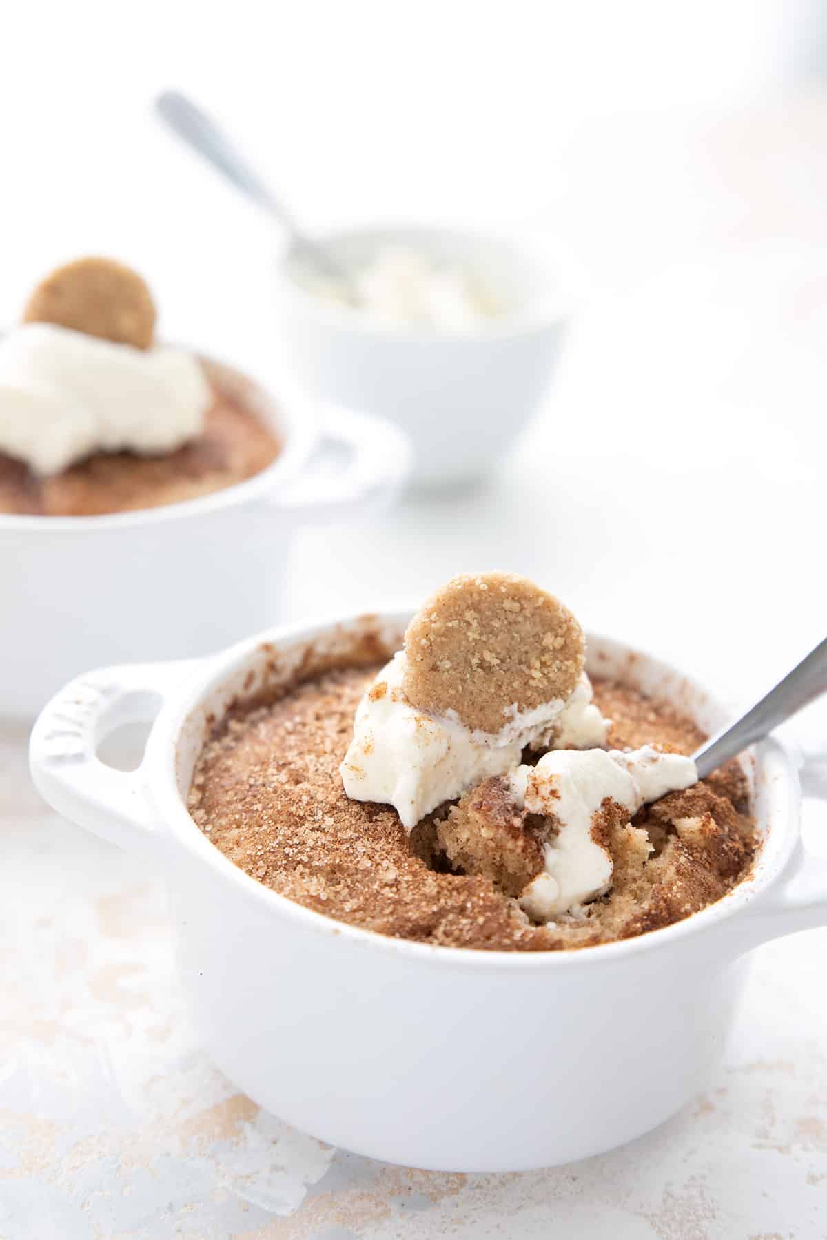 Keto mug cake in a white ramekin, with whipped cream and a mini snickerdoodle cookie on top.