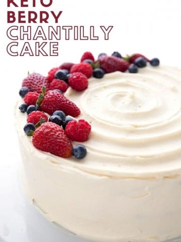 Titled Image of a Keto Chantilly Cake on a white cake platter, topped with fresh berries
