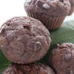 Close up shot of keto chocolate zucchini muffins in a pile on a white table.
