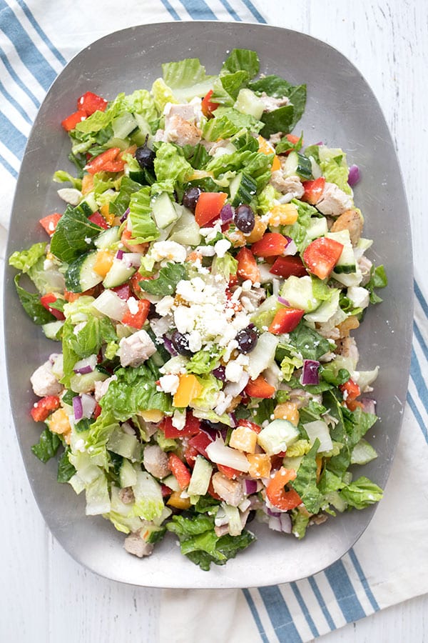 Top down photo of Greek Chopped Salad on a pewter platter, over a blue and white striped napkin