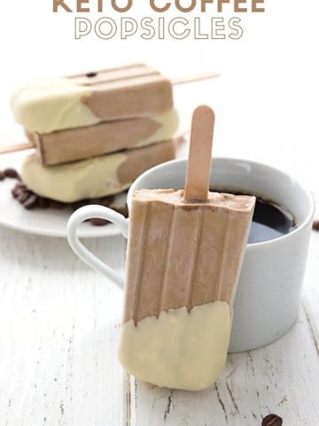 Titled image of keto coffee popsicles on a white table, with one popsicle leaning against a cup of coffee