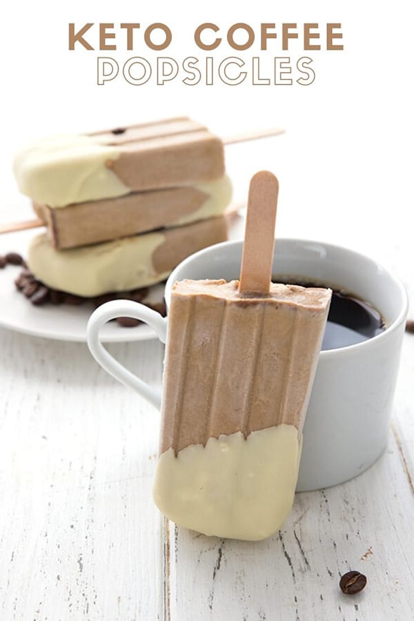 Titled image of keto coffee popsicles on a white table, with one popsicle leaning against a cup of coffee
