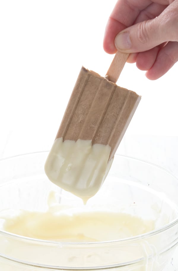 A coffee popsicle being dipped into melted white chocolate