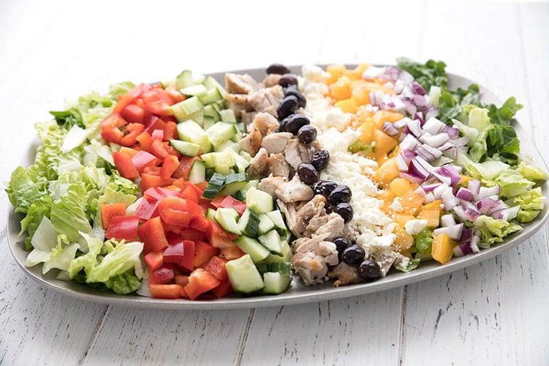 A pewter platter layered with the ingredients for chopped Greek chicken salad