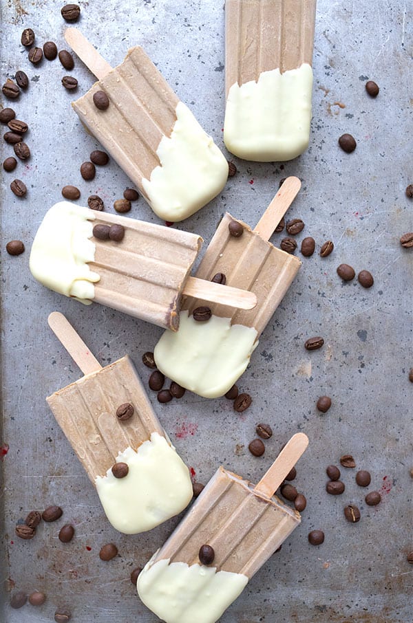 Top down photo of white chocolate dipped keto coffee popsicles with coffee beans strewn around.