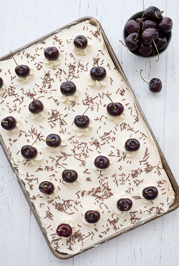 Top down photo of keto Black Forest sheet cake with fresh cherries and chocolate sprinkles on a white wooden table.