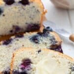 Titled image of a slice of keto blueberry bread with butter on it, on a white table.