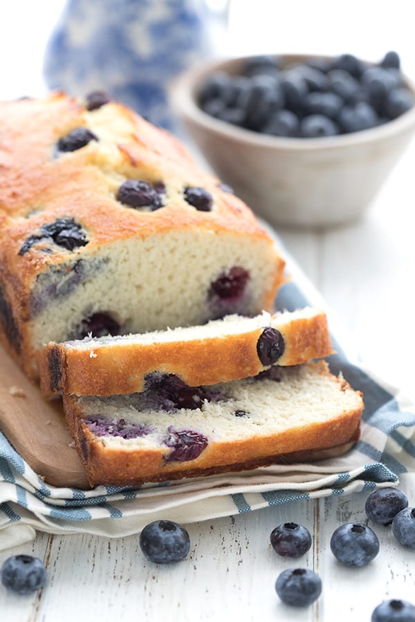 Close up shot of keto blueberry bread, sliced on a cutting board, with blueberries all around.