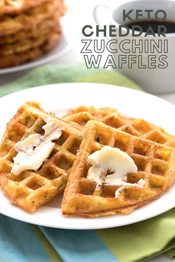 Titled image of keto zucchini waffles on a plate, slathered with butter, over a green napkin. A cup of coffee in the background.