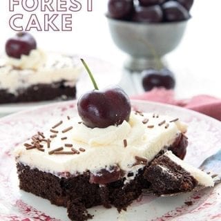 Titled image of a piece of keto Black Forest Cake on a red patterned plate, with a bowl of cherries in the background