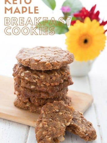 Titled image of keto breakfast cookies. The cookies sit on a wooden cutting board in a stack, in front of a vase of flowers.