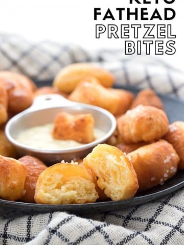 Titled image: a close up of keto pretzel bites on a black plate over a checked napkin. The front bite is broken open to show the inside.