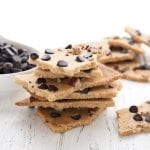 Keto cookie brittle piled around a white table with a bowl of chocolate chips.