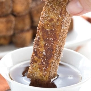 Close up of a hand dipping a keto pumpkin french toast stick into sugar-free syrup.